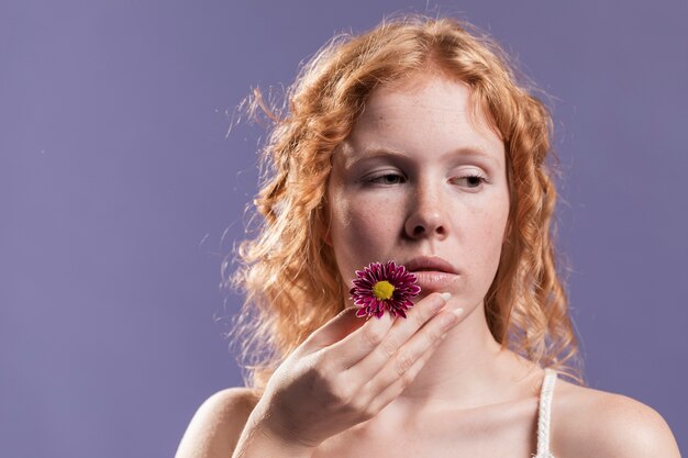 Vista frontal de la mujer pelirroja sosteniendo una flor cerca de su boca con espacio de copia