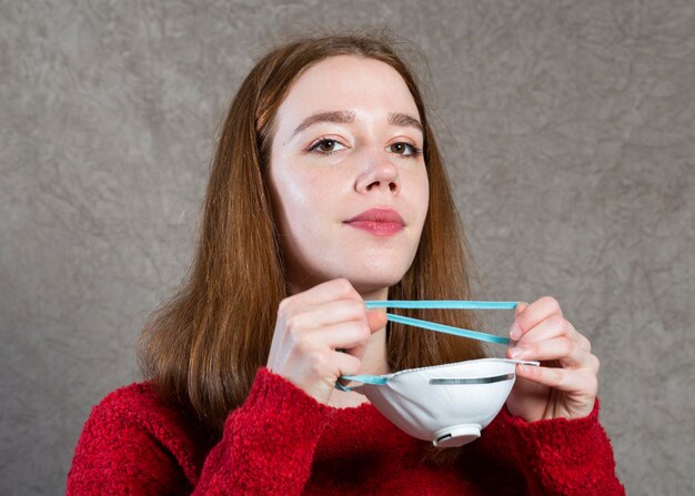 Vista frontal de la mujer poniéndose una máscara médica en la cara para protección