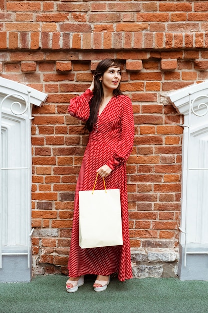 Vista frontal de la mujer posando afuera con bolsas de la compra.