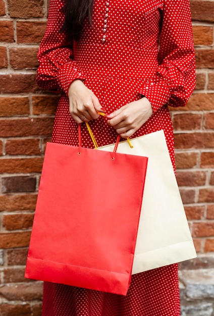 Vista frontal de la mujer posando afuera mientras sostiene varias bolsas de la compra.