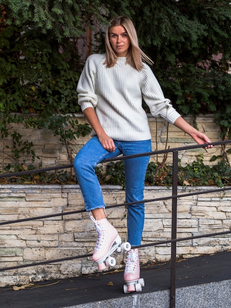 Vista frontal de la mujer posando en jeans y patines detrás de la barandilla