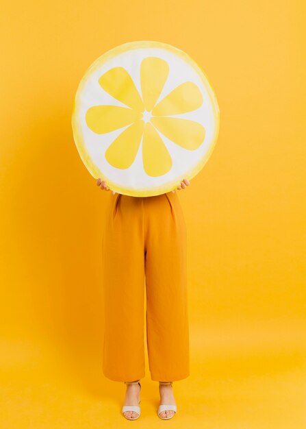 Vista frontal de la mujer posando mientras se cubre la cabeza con decoración de rodaja de limón