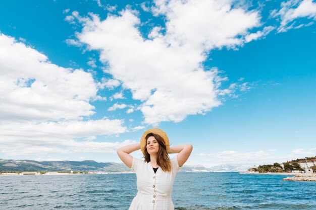 Vista frontal de la mujer posando en el océano con nubes en el cielo