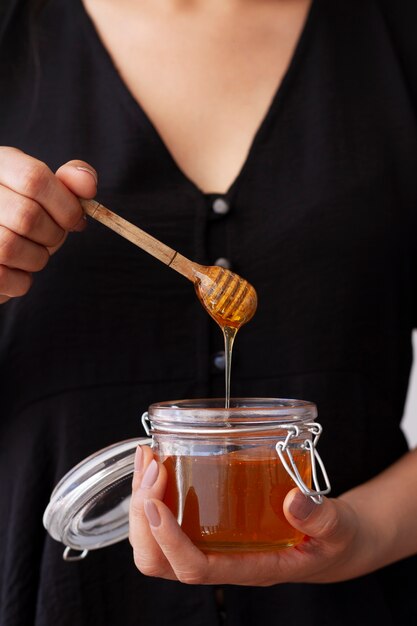 Vista frontal de la mujer que sostiene el tarro con miel y cucharón de miel