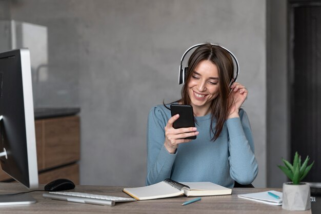 Vista frontal de la mujer que trabaja en el campo de los medios de comunicación con teléfonos inteligentes y auriculares