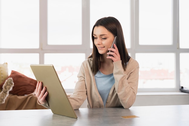 Vista frontal de la mujer que trabaja en casa con teléfono inteligente y tableta