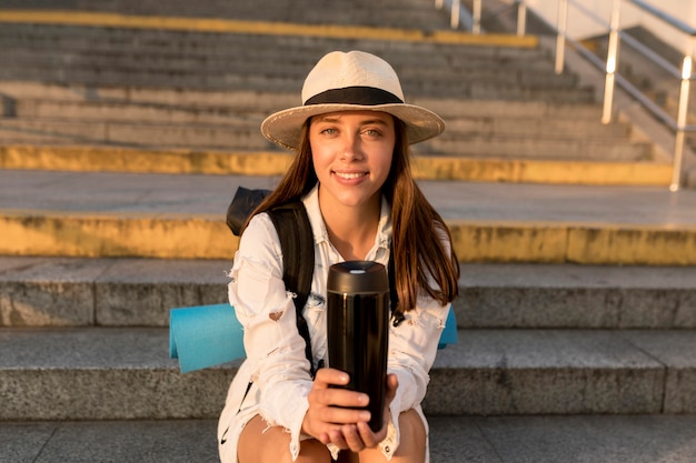 Foto gratuita vista frontal de la mujer que viaja con sombrero y mochila con termo