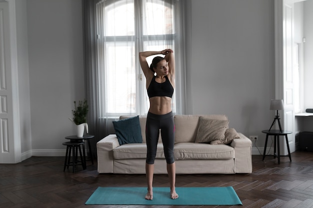 Vista frontal de la mujer en ropa deportiva que se extiende sobre estera de yoga