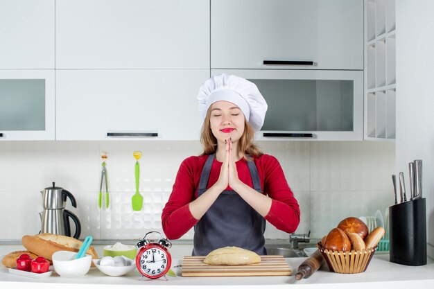 Vista frontal mujer rubia con sombrero de cocinero uniendo sus manos en la cocina