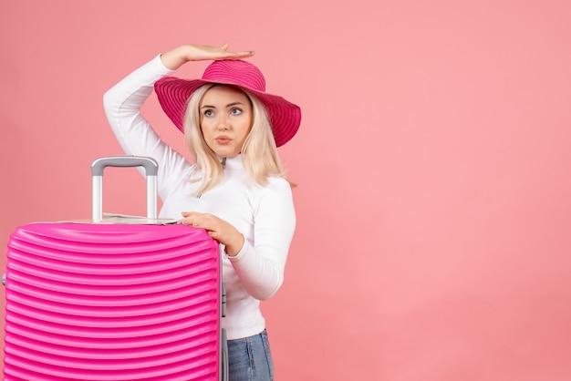 Vista frontal mujer rubia con sombrero panamá rosa sosteniendo su maleta