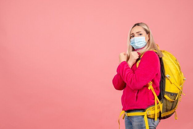 Vista frontal mujer rubia viajera con mochila amarilla con máscara cruzando las manos