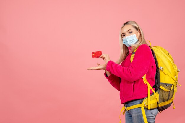 Vista frontal mujer rubia viajera con mochila amarilla con tarjeta de tenencia de máscara