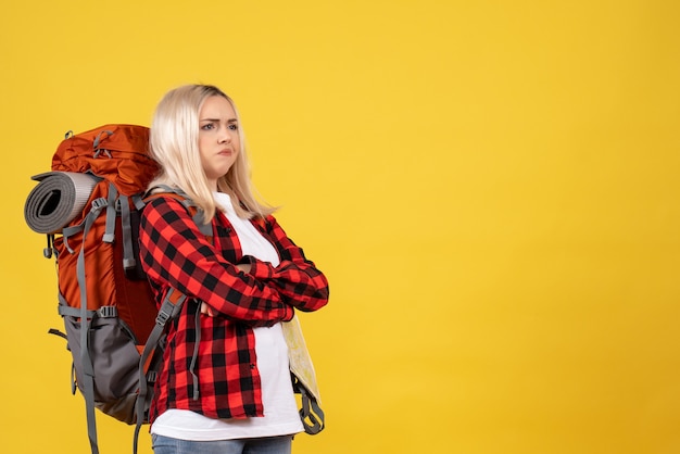 Foto gratuita vista frontal mujer rubia viajera con su mochila cruzando las manos de pie sobre la pared amarilla