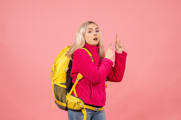 Vista frontal mujer rubia viajero con mochila amarilla apuntando con los dedos hacia arriba