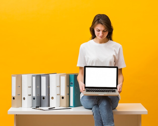 Vista frontal de la mujer sentada en el escritorio y sosteniendo portátil