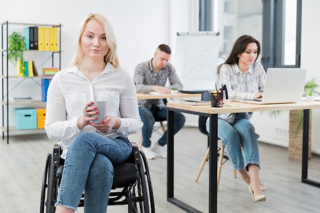 Vista frontal de la mujer en silla de ruedas posando en el trabajo mientras sostiene la taza