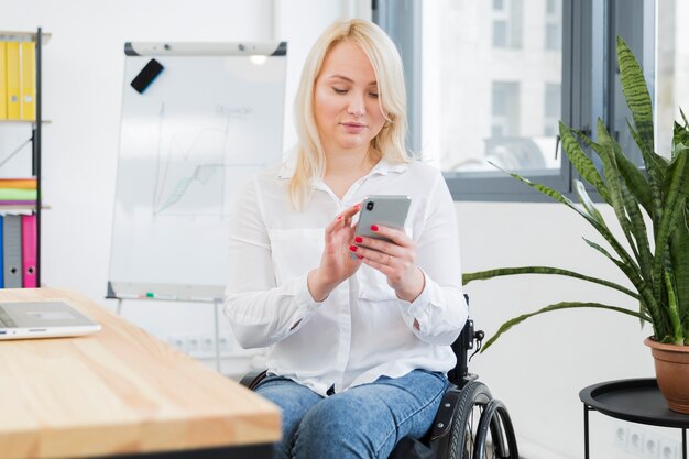 Vista frontal de la mujer en silla de ruedas con smartphone