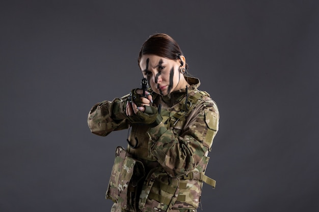 Vista frontal de la mujer soldado apuntando con pistola en la pared oscura de camuflaje