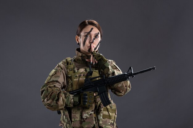 Vista frontal mujer soldado en camuflaje con ametralladora en pared gris
