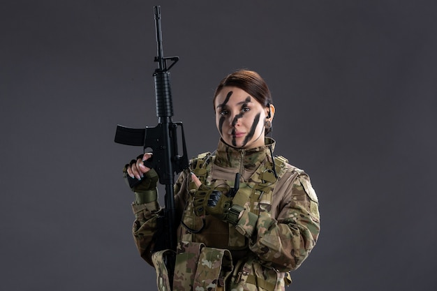 Vista frontal mujer soldado en camuflaje con ametralladora en la pared oscura