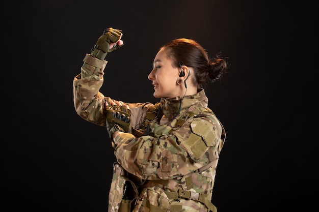 Vista frontal de la mujer soldado en camuflaje mostrando su fuerza en la pared negra