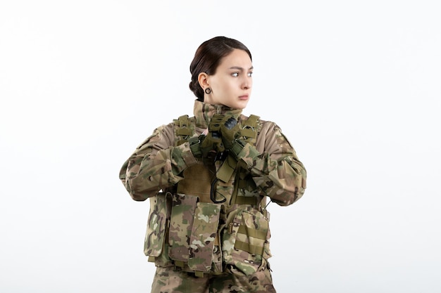 Vista frontal de la mujer soldado en camuflaje en la pared blanca