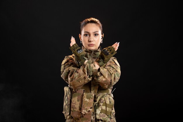 Vista frontal de la mujer soldado en camuflaje en la pared negra