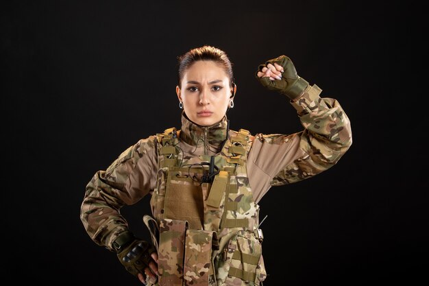 Vista frontal de la mujer soldado en camuflaje en la pared negra