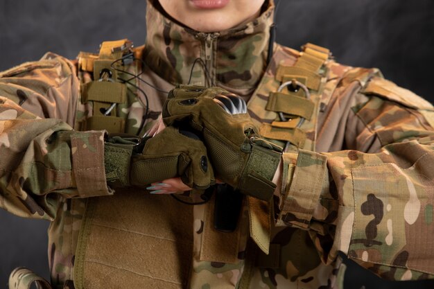 Vista frontal de la mujer soldado en camuflaje en la pared oscura