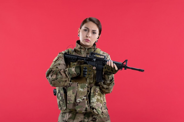 Vista frontal mujer soldado en camuflaje con pared roja de ametralladora