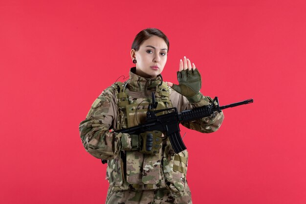 Vista frontal mujer soldado en camuflaje con pared roja de ametralladora