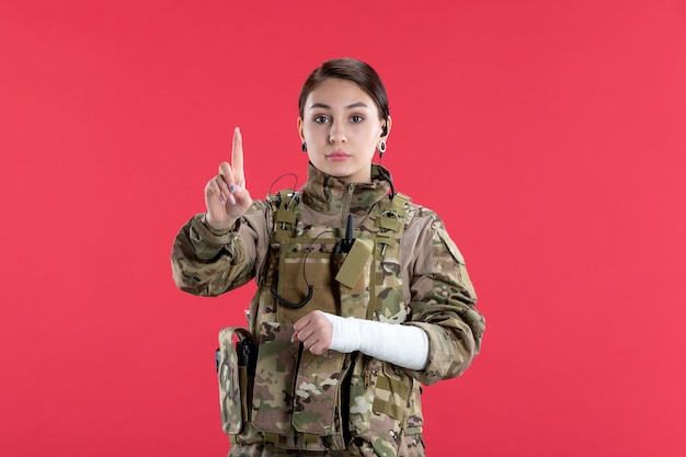 Vista frontal mujer soldado en camuflaje con pared roja del brazo roto