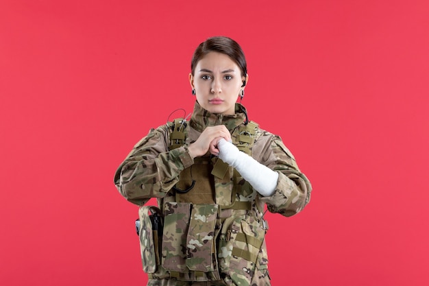 Vista frontal mujer soldado en camuflaje con pared roja del brazo roto