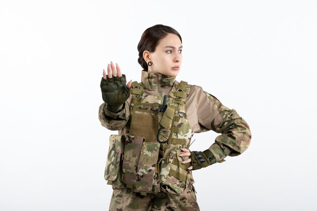 Vista frontal de la mujer soldado en camuflaje pidiendo detener la pared blanca