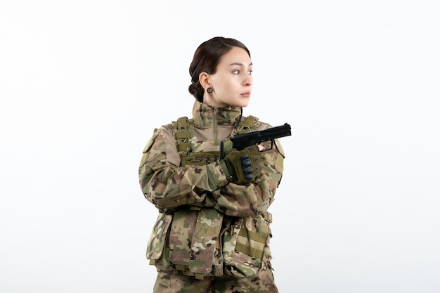 Vista frontal mujer soldado en camuflaje con pistola en pared blanca