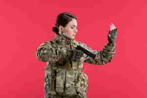 Foto gratuita vista frontal de la mujer soldado en camuflaje sosteniendo la pistola en la pared roja