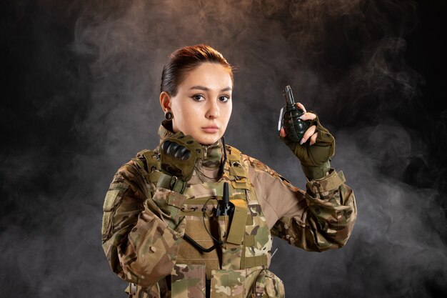 Vista frontal de la mujer soldado con granada en uniforme sobre pared negra