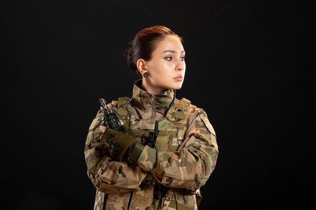 Vista frontal de la mujer soldado con granada en uniforme sobre pared negra