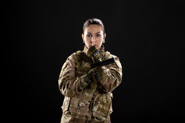 Vista frontal mujer soldado con pistola en uniforme sobre pared negra