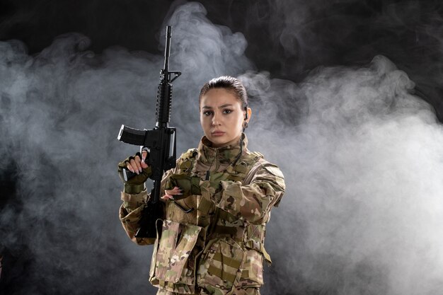 Vista frontal mujer soldado en uniforme comprobando el tiempo en la pared negra