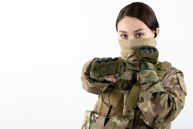 Vista frontal de la mujer soldado en uniforme militar en la pared blanca