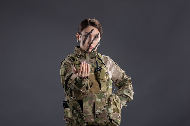 Vista frontal de la mujer soldado en uniforme militar en la pared oscura