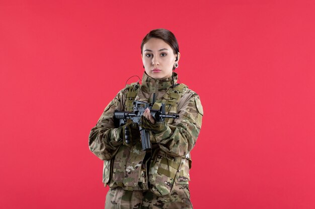 Vista frontal mujer soldado en uniforme militar con pared roja de ametralladora