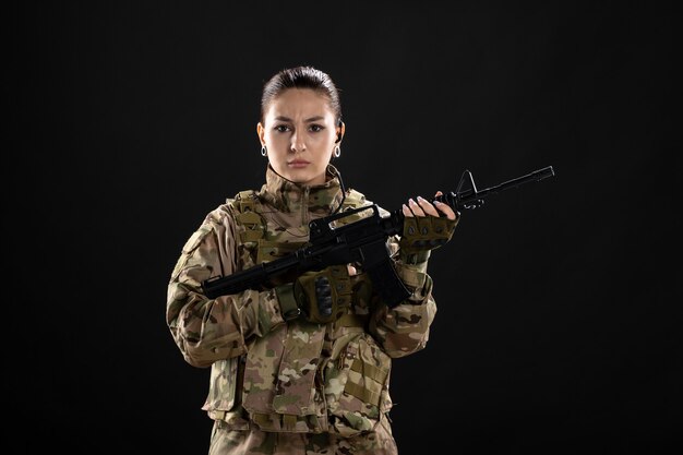 Vista frontal de la mujer soldado en uniforme con el objetivo de rifle en la pared negra