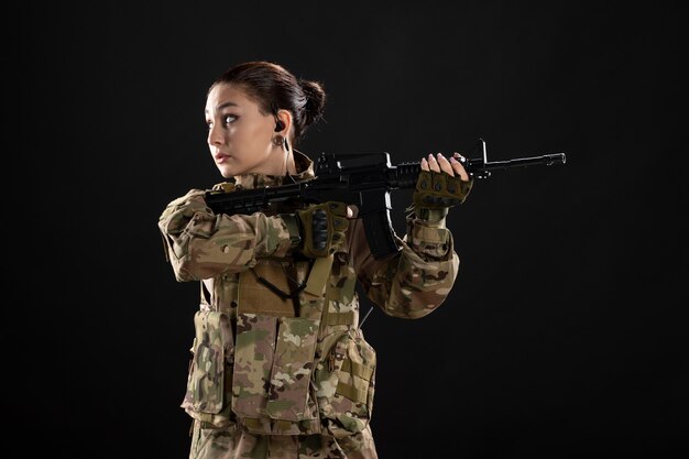 Vista frontal de la mujer soldado en uniforme con el objetivo de rifle en la pared negra