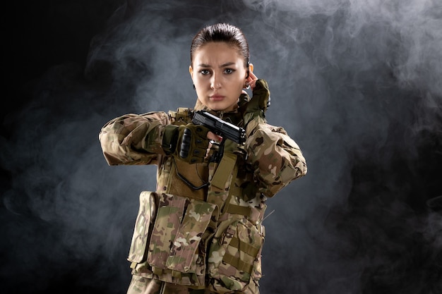 Vista frontal mujer soldado en uniforme con pistola en pared negra