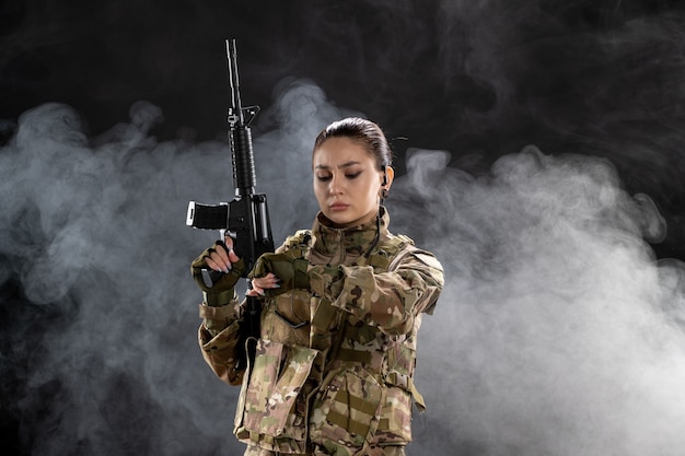 Vista frontal mujer soldado en uniforme sosteniendo rifle en pared negra