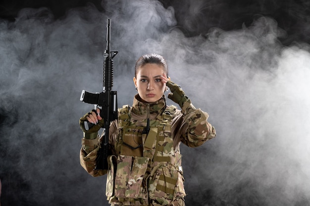 Vista frontal mujer soldado en uniforme sosteniendo rifle en pared negra