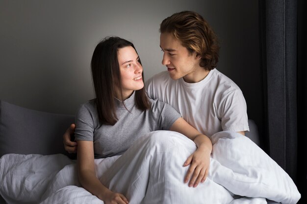 Vista frontal de la mujer sonriendo al novio mientras está sentado en la cama