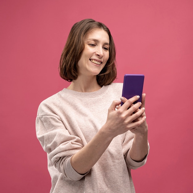 Foto gratuita vista frontal de la mujer sonriendo y mirando el teléfono inteligente